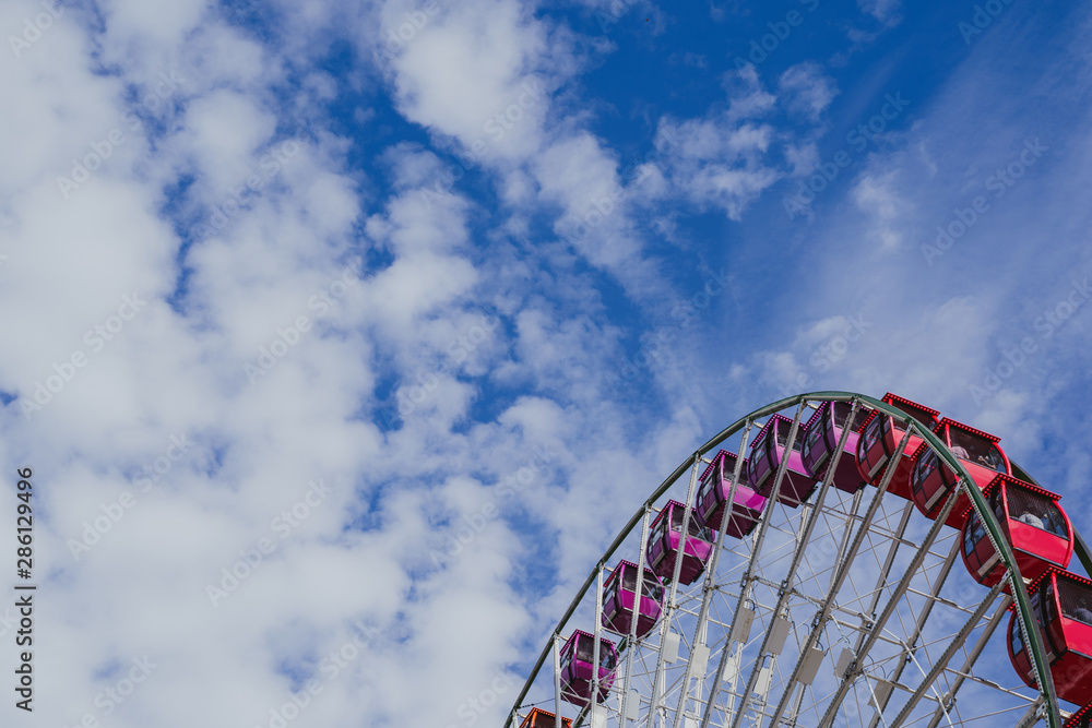Negative space, artistic composition of a colorful large ferris wheel against a partly cloudy sky