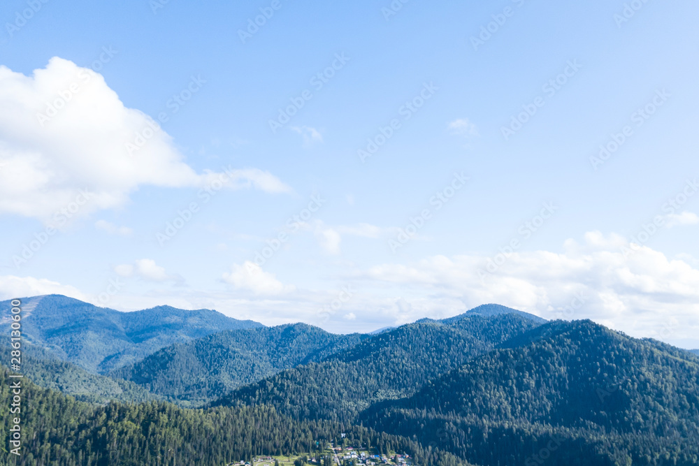 Obraz premium landscape of the ridge covered with green trees and view a valley flooded with sunlight ,pasture, with dense clouds in the sky. summer day in the mountains of the Altai