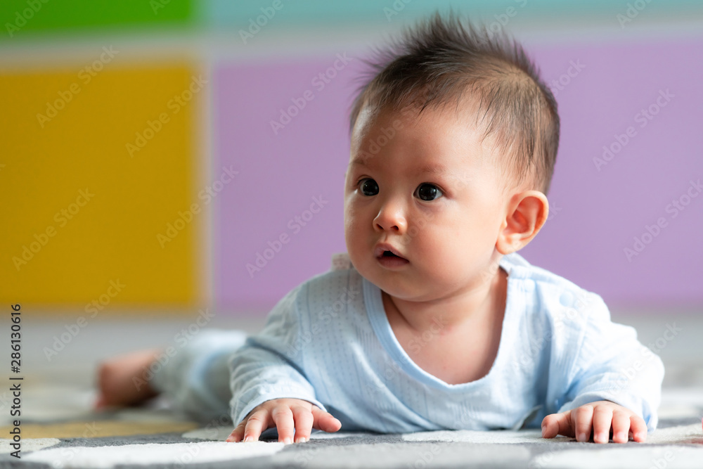 Portrait of young asian baby toddler laying on floor on carpet with colorful background. Looking to the left and smile. Portrait of young asian baby toddler laying on floor on carpet with colorful background. Looking to the left and smile.