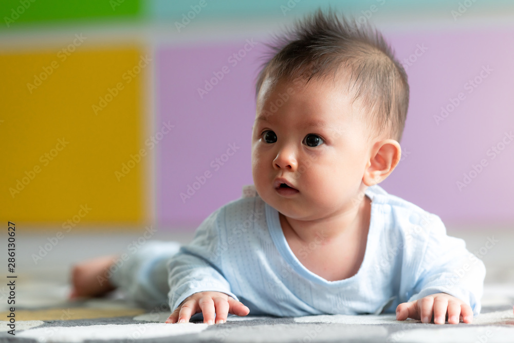 Portrait of young asian baby toddler laying on floor on carpet with colorful background. Looking to the right, innocent look. With light leak effect. Portrait of young asian baby toddler laying on floor on carpet with colorful background. Looking to the right, innocent look. With light leak effect.