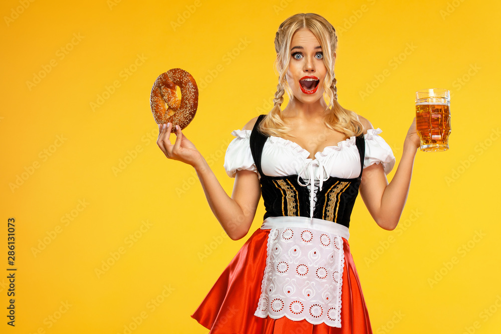 Young sexy Oktoberfest girl waitress, wearing a traditional Bavarian or  german dirndl, serving big beer mugs with drink and bretzel, isolated on  yellow background. Wow emotion. Stock-Foto | Adobe Stock