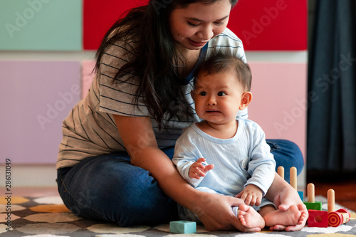 Young asian mother playing with her male toddler in living room. Happy smile.
