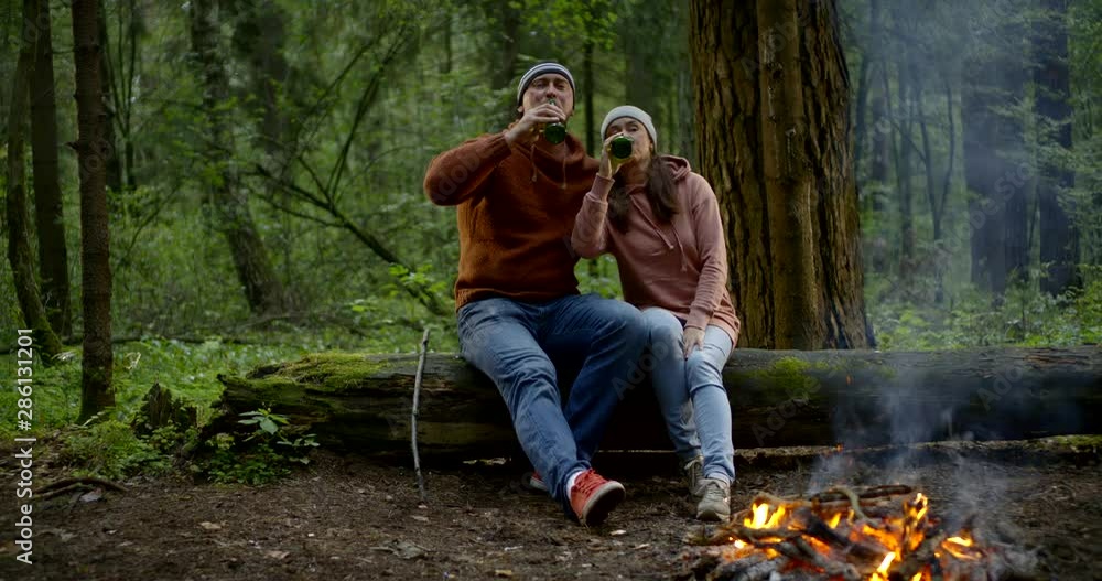 adult man and woman in love are drinking beer from bottles and kissing on picnic in forest adult man and woman in love are drinking beer from bottles and kissing on picnic in forest