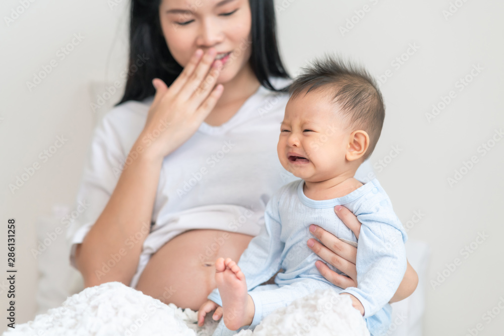 Asian male toddler sitting with his pregnant mother in bedroom. Crying face. Asian male toddler sitting with his pregnant mother in bedroom. Crying face.