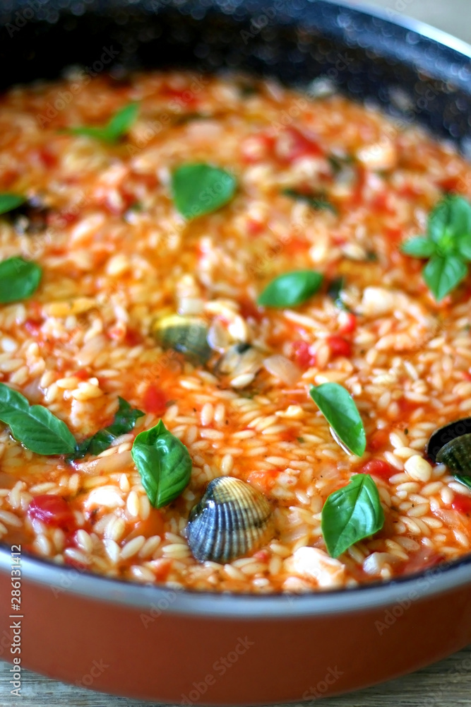 Orzo pasta, cooked with tomato sauce, vegetables and seafood, served on a table. Selective focus. Orzo pasta, cooked with tomato sauce, vegetables and seafood, served on a table. Selective focus.