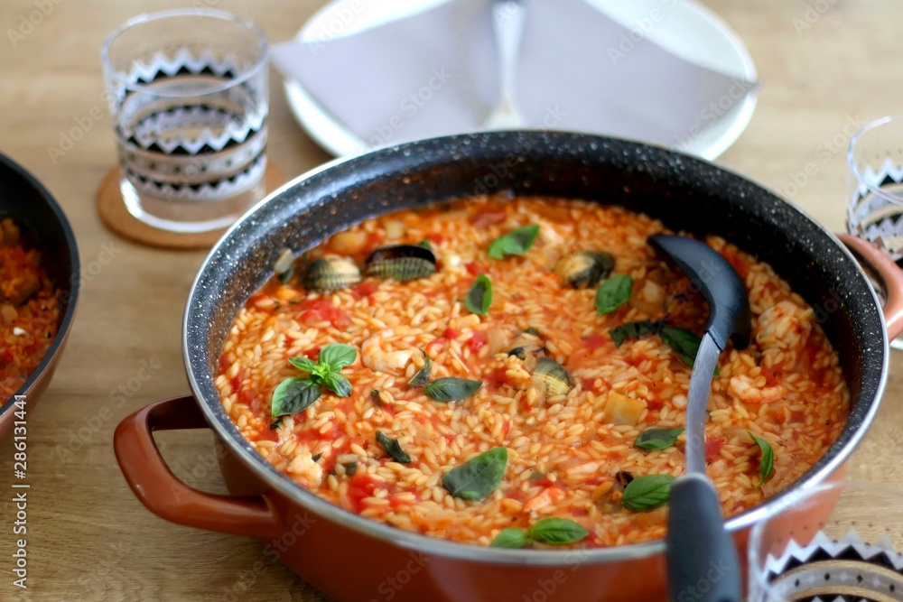Orzo pasta, cooked with tomato sauce, vegetables and seafood, served on a table. Selective focus. Orzo pasta, cooked with tomato sauce, vegetables and seafood, served on a table. Selective focus.
