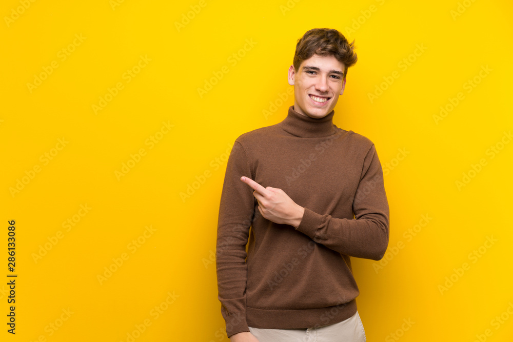 Handsome young man over isolated yellow background pointing to the side to present a product Handsome young man over isolated yellow background pointing to the side to present a product