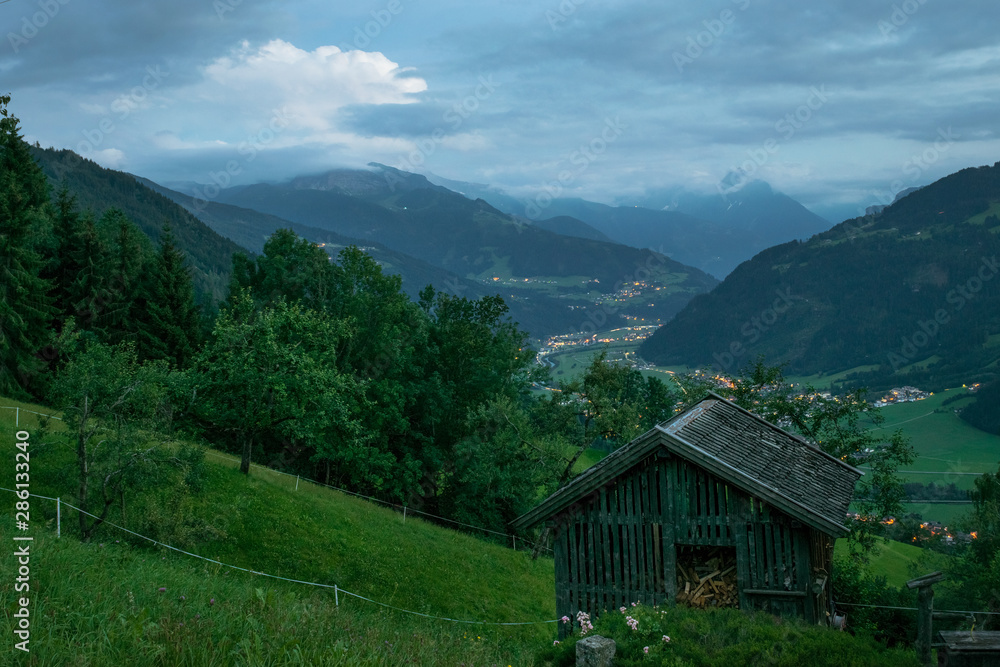 Old hut in the mountains of the Alps with beautiful view over the valley at dusk. A thunderstorm rumbles in the distance.