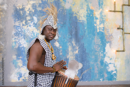 Fototapeta African artist in traditional clothes playing djembe drum