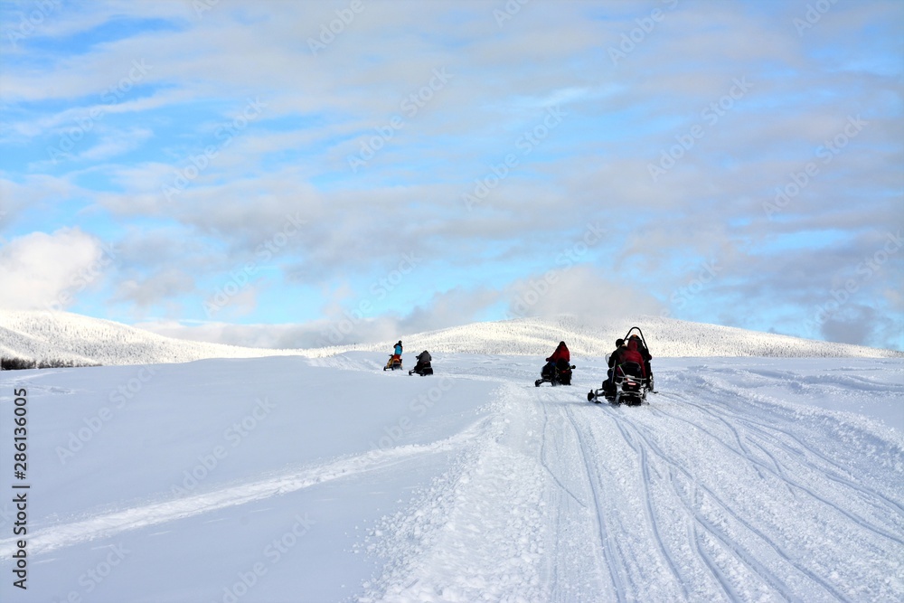 people driving snowmobiles on a snowy field
