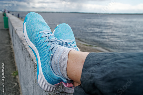 Sporty woman wears blue tying the laces on blue running shoes while taking break between training outside.