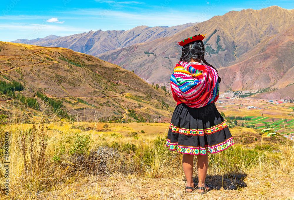 An indigenous Peruvian Quechua lady looking at the Andes Mountain Range in the Inca ruin of Tipon in the region of Cusco, Peru. Square format. - obrazy, fototapety, plakaty 
