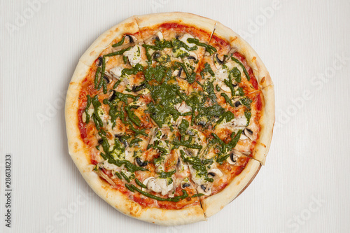 Italian pizza with chicken and mushrooms, on a white wooden table, poured with pesto