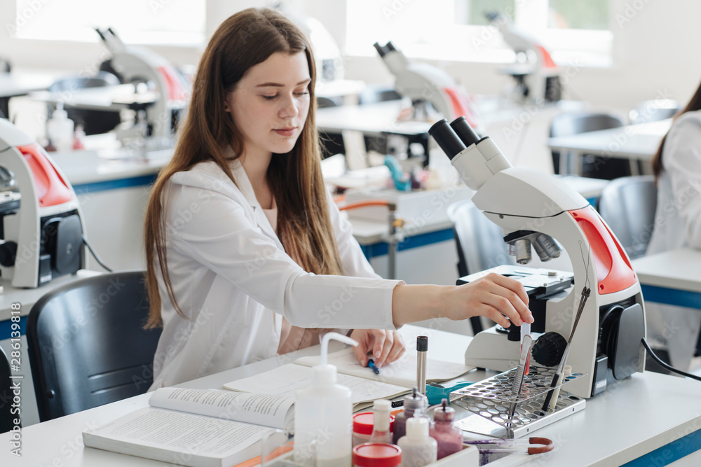Young female researcher in white coat working in lab with a laboratory sample Young female researcher in white coat working in lab with a laboratory sample