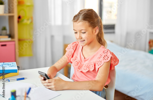 children, education and technology concept - happy student girl using smartphone at home