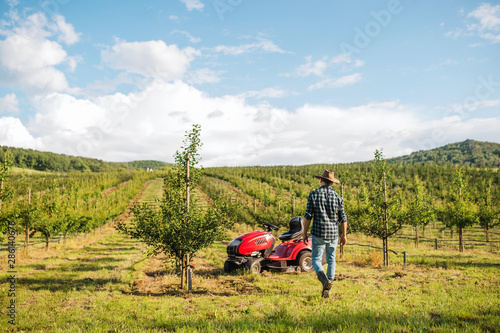 Rear view of farmer walking outdoors towards mini tractor in orchard.