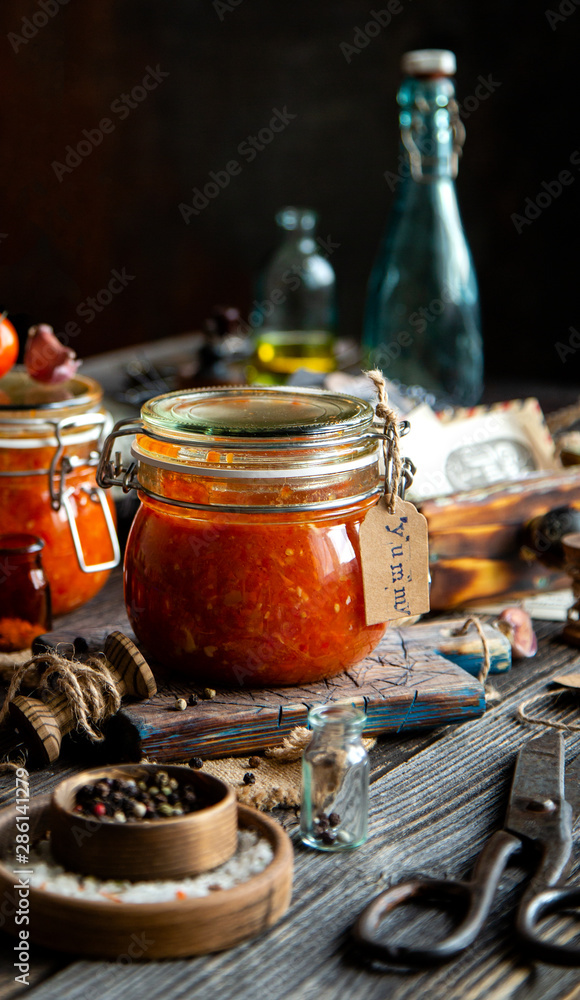 Homemade canned hot tomato sauce adjika in two glass jars standing on wooden board