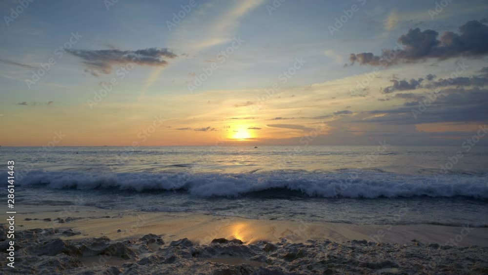 View from tropical beach of sunset in ocean with blue water and big waves under beautiful yellow sky View from tropical beach of sunset in ocean with blue water and big waves under beautiful yellow sky
