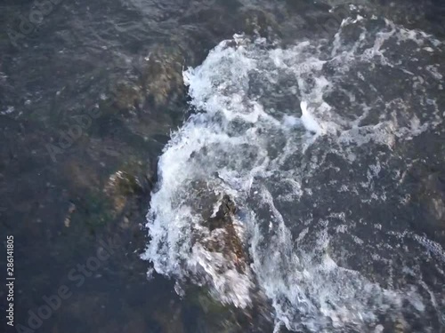 Water stream flows across the stones. River flowing close up.