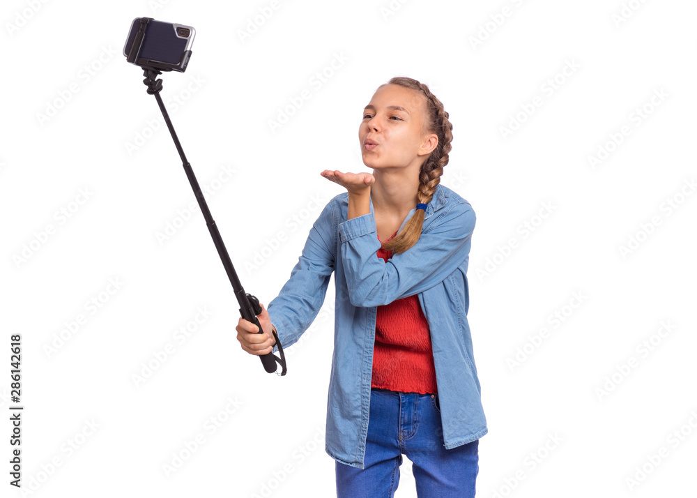 Happy teen girl making selfie with stick and sending an air kiss. Teenager posing to smartphone on selfie stick, isolated on white background. Child taking selfie on mobile phone for social network. Happy teen girl making selfie with stick and sending an air kiss. Teenager posing to smartphone on selfie stick, isolated on white background. Child taking selfie on mobile phone for social network.
