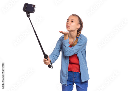 Happy teen girl making selfie with stick and sending an air kiss. Teenager posing to smartphone on selfie stick, isolated on white background. Child taking selfie on mobile phone for social network.