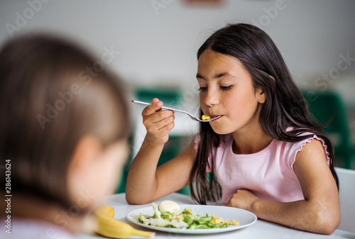 Small school girlas in canteen, eating lunch.