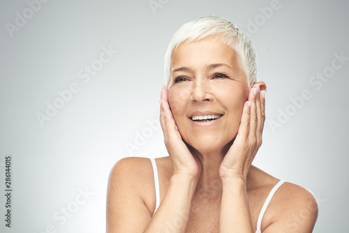 Beautiful smiling senior woman with short gray hair posing in front of gray background. Beauty photography.