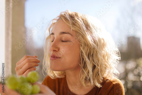 Portrait of blond young woman eating green grapes
