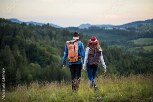 Rear view of young tourist couple travellers with backpacks hiking in nature.