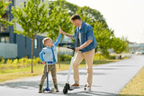 family, leisure and fatherhood concept - happy father spending time with little son riding scooters and making high five in city