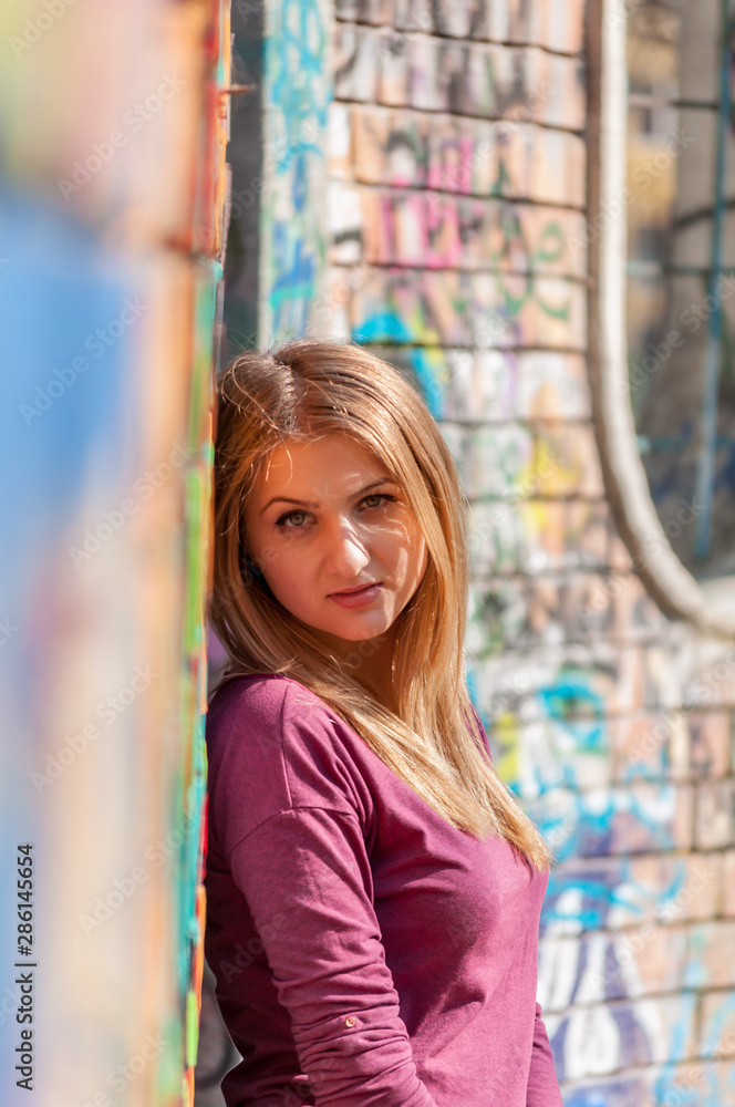 Naklejka premium Outdoors portrait of a woman, leaning against a colored wall