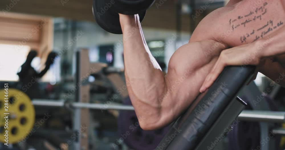 Details bodybuilding man doing exercises in a large spacious gym portrait baked biceps workout lifting up the dumbbell Details bodybuilding man doing exercises in a large spacious gym portrait baked biceps workout lifting up the dumbbell