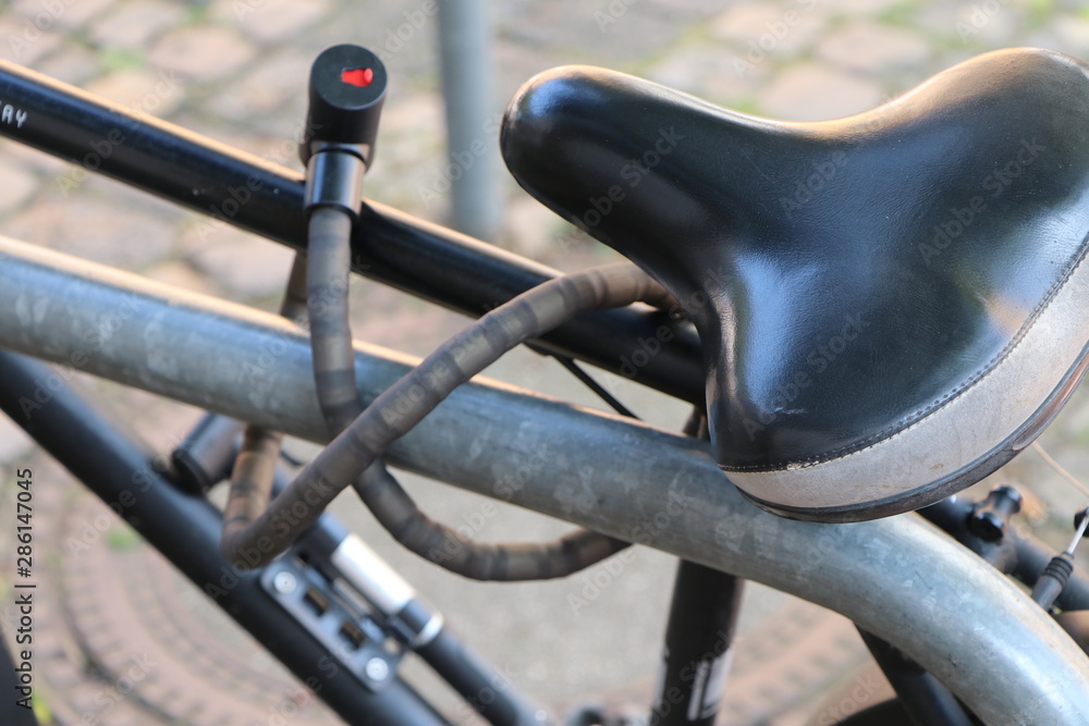 Bike locked to a metal bicycle stand. Closeup of saddle and bicycle lock. Bike locked to a metal bicycle stand. Closeup of saddle and bicycle lock.