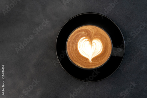 Top view of hot coffee cappuccino latte art heart shape foam in black cup on dark table background