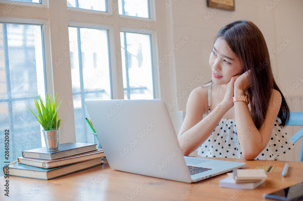 asian woman relaxing and using laptop on wooden table  next to the window in the home,  working woman concept.