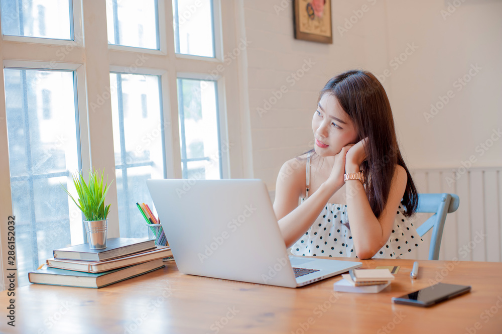 asian woman relaxing and using laptop on wooden table next to the window in the home, working woman concept. asian woman relaxing and using laptop on wooden table next to the window in the home, working woman concept.