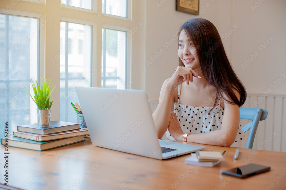 asian woman relaxing and using laptop on wooden table next to the window in the home, working woman concept. asian woman relaxing and using laptop on wooden table next to the window in the home, working woman concept.