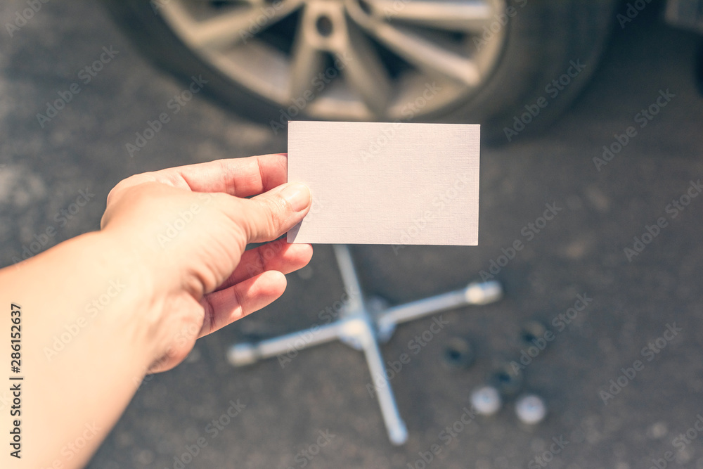 woman crouching near her car with  punctured wheel. girl holding business card with data of isurance company. Concept. mock up - obrazy, fototapety, plakaty 