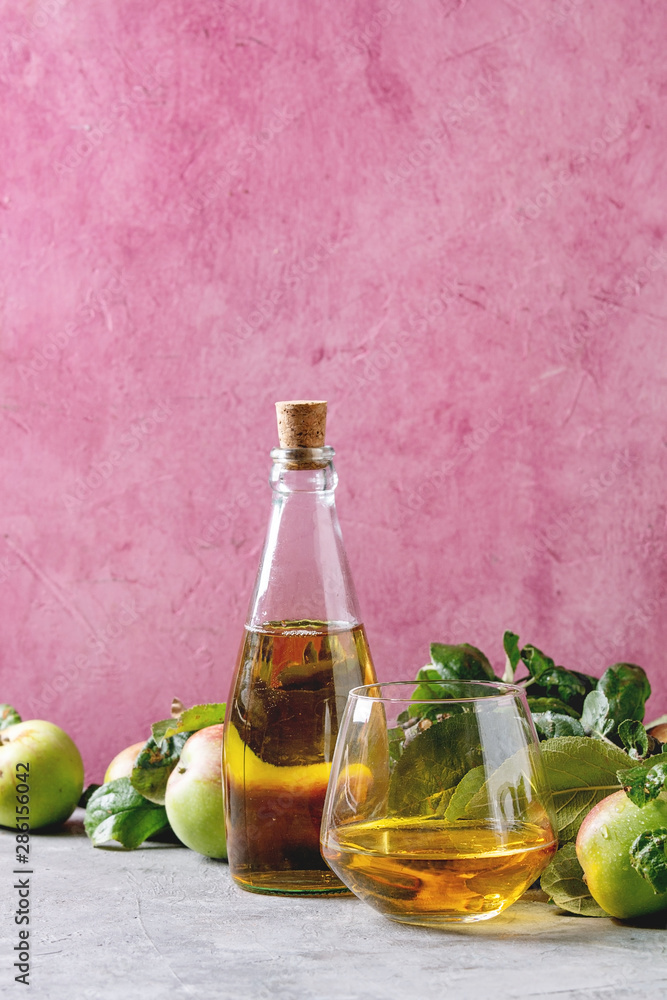 Bottle ang glass of apple juice with garden apples with leaves and branches on table with pink background. Autumn home harvesting. Bottle ang glass of apple juice with garden apples with leaves and branches on table with pink background. Autumn home harvesting.
