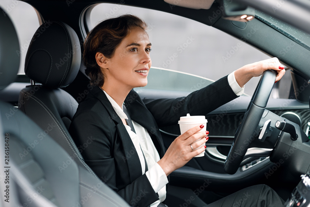 Businesswoman going to office in her car. Side view of female driver holding a coffee.
