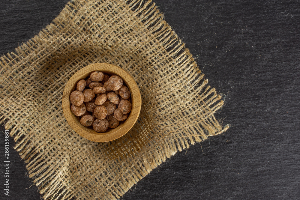 Lot of whole chocolate ball breakfast cereals in wooden bowl on jute cloth flatlay on grey stone