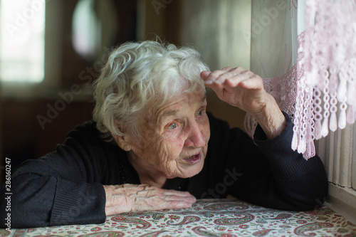 Old lady looks out the window of her house.