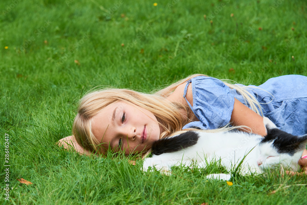 Child blond girl playing and stroking with cat on grass at summer Child blond girl playing and stroking with cat on grass at summer