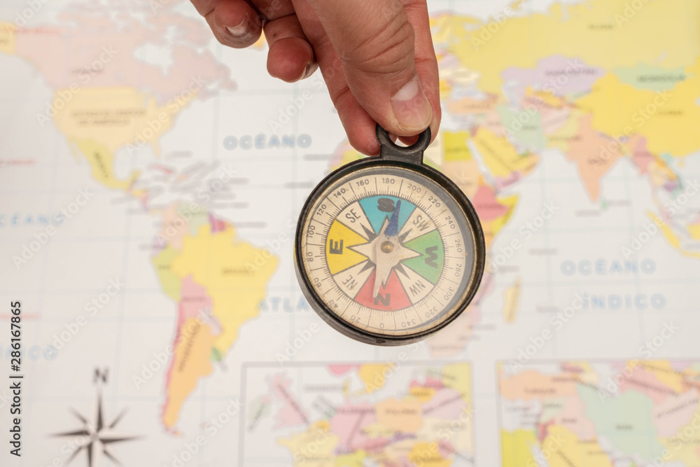 Woman hand holding a colorful compass with a map as background