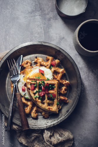 Belgian crispy waffles with fried egg, tomatoes and latte coffee on grey table