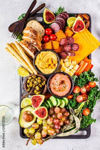 Meat and cheese appetizer platter. Sausage, cheese, hummus, vegetables, fruits and bread on black tray.