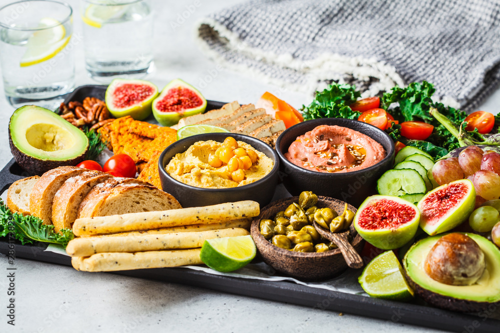 Vegan appetizer platter. Hummus, tofu, vegetables, fruits and bread on black tray, copy space.