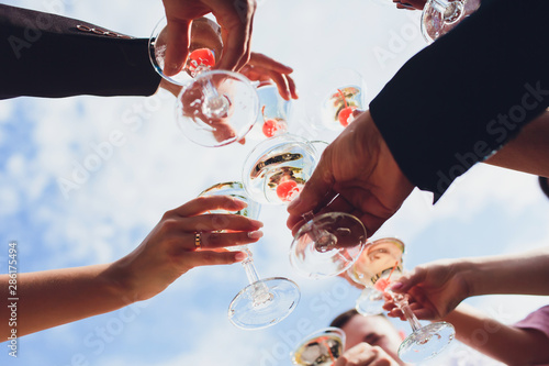 Close up shot of group of people clinking glasses with wine or champagne in front of bokeh background.