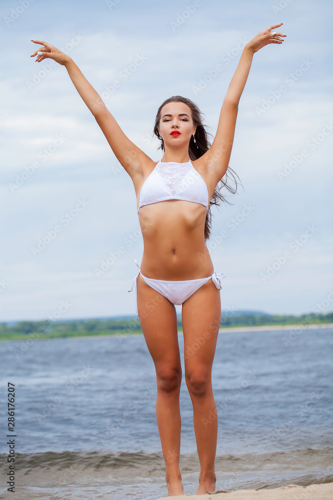 Portrait of a young beautiful girl in a white bathing suit posing on the background of the Volga river