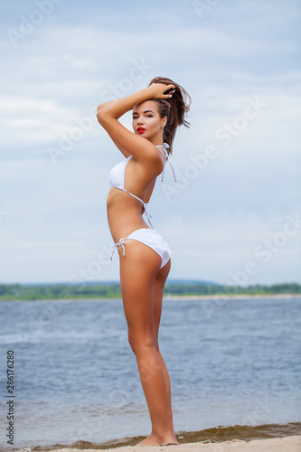 Portrait of a young beautiful girl in a white bathing suit posing on the background of the Volga river